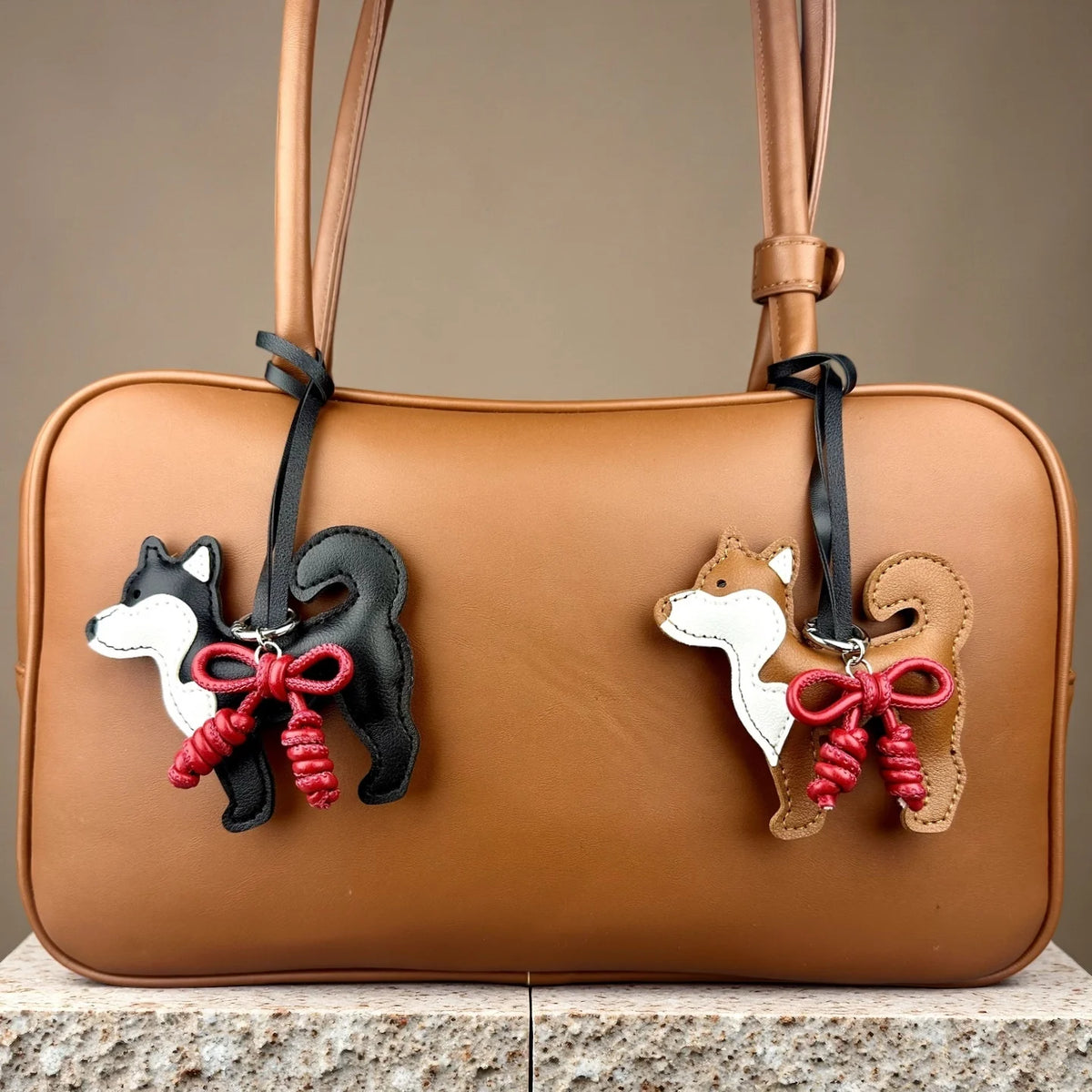 A tan leather handbag featuring a black and white Shiba Inu charm with a red braided bow.