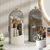 A clear glass rotating makeup brush holder with a dustproof lid displaying various makeup brushes and tools.