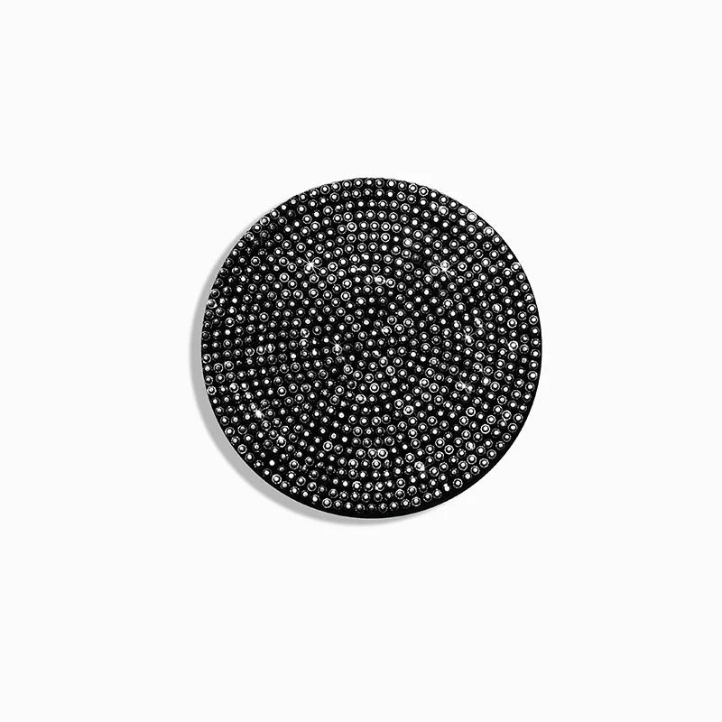 A circular black coaster with a textured, diamond-like pattern.