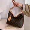 A hand holds a brown leather tote bag with a gold chain strap and a small leather tag against a white background.