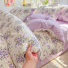 A close-up of a lavender floral duvet cover set with matching pillowcases and a folded duvet on a bed.