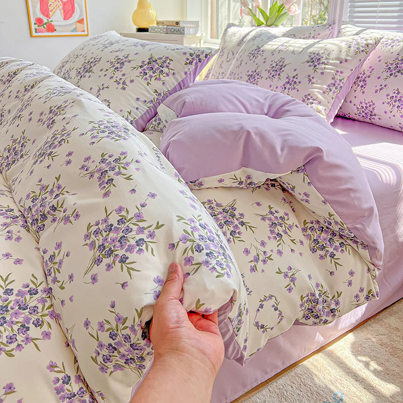 A close-up of a lavender floral duvet cover set with matching pillowcases and a folded duvet on a bed.