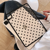 A beige polka dot protective case for an iPad is shown resting on a person's jeans and white fabric.