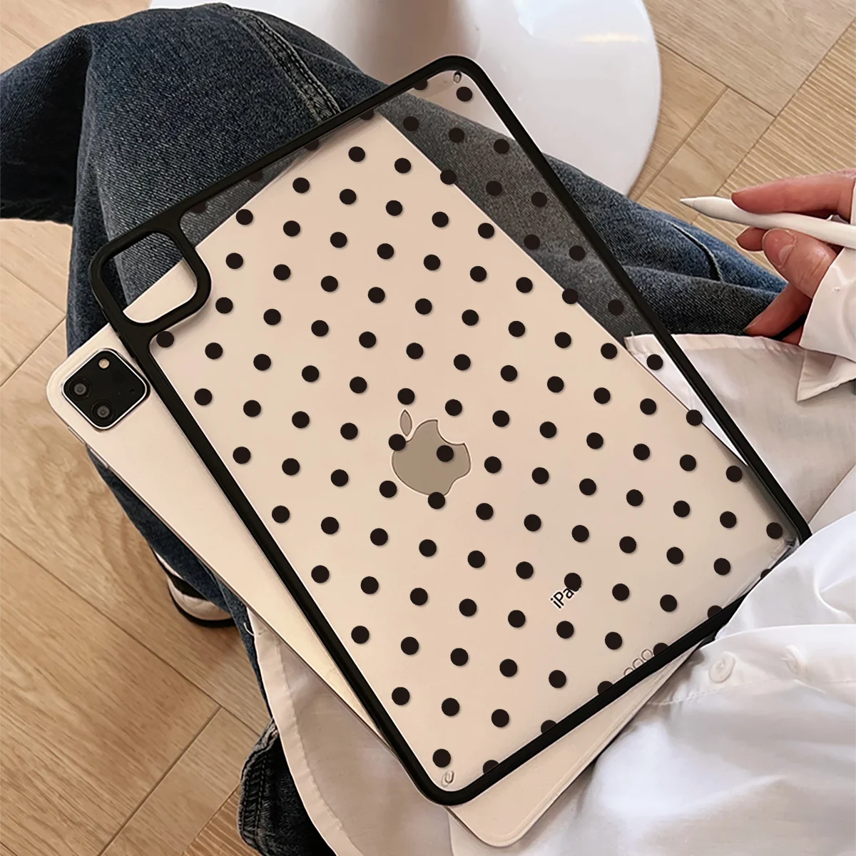 A beige polka dot protective case for an iPad is shown resting on a person's jeans and white fabric.