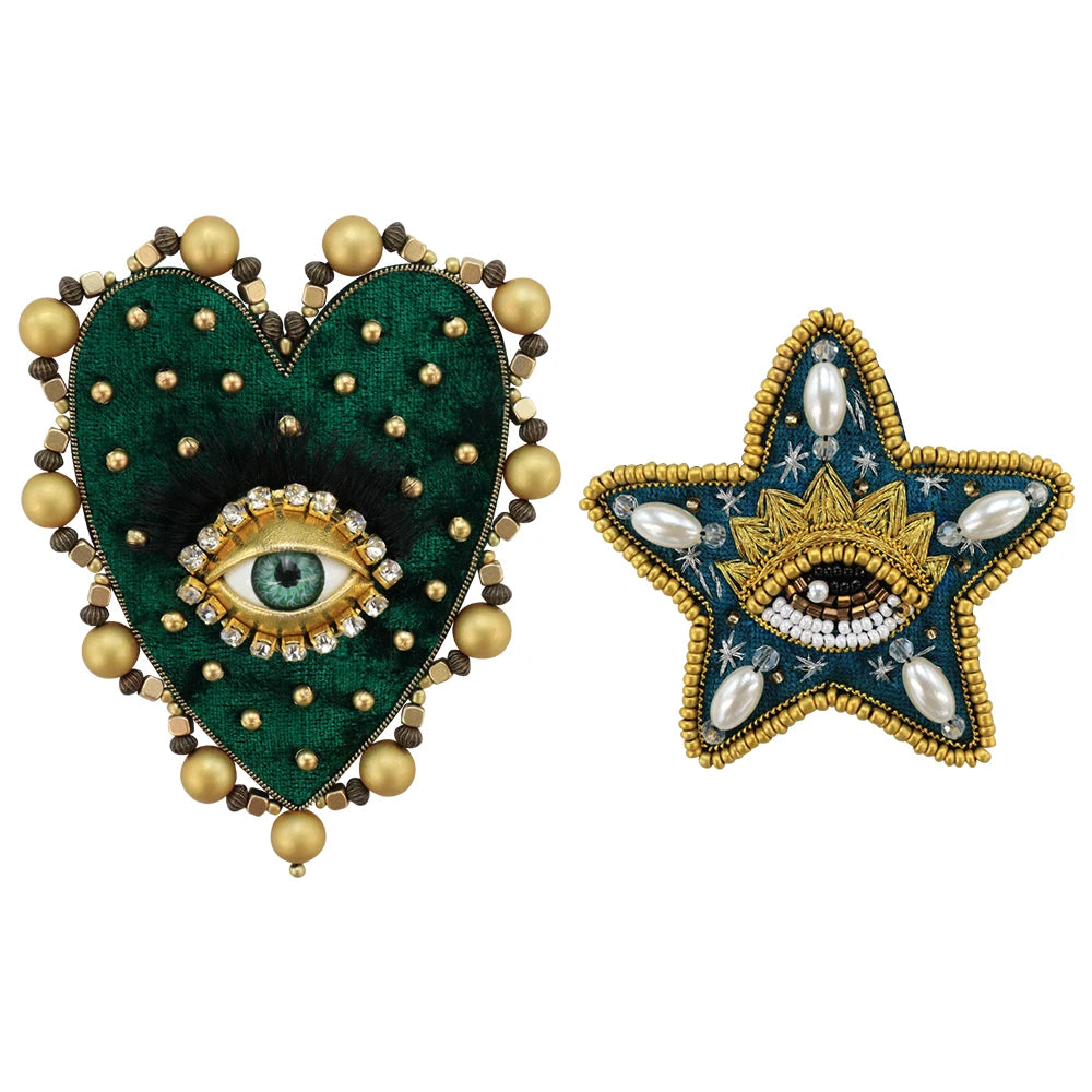 A heart-shaped patch adorned with green fabric, gold beads, and a central iridescent eye design.