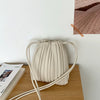A beige pleated faux leather crossbody bag resting on a wooden surface.