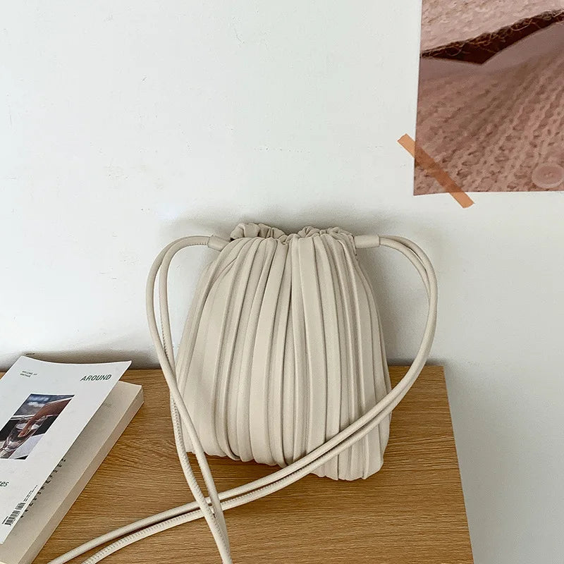 A beige pleated faux leather crossbody bag resting on a wooden surface.