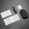 A black compact RFID wallet is shown next to a stack of US dollar bills and several white plastic cards on a dark surface.