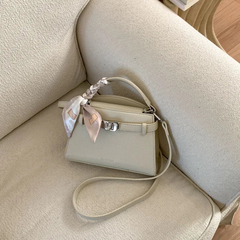 Elegante beigefarbene PU-Leder-Clutch mit geflochtenem Riem auf cremefarbener Polsterung.