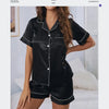 A woman models a black satin pajama set consisting of a button-down top and matching shorts.