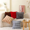 A collection of soft plush decorative pillows in shades of brown, red, and gray resting on a light-colored sofa.