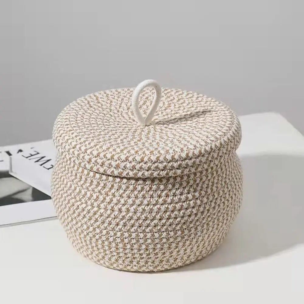Beige handgewebter Baumwoflaschenkorb mit Deckel auf weißer Fläche.