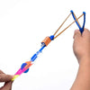 A hand holds an LED glowing flying arrow toy with a rubber band launcher, showing the colorful arrow and launching mechanism.