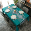 A teal tablecloth set for a dining table featuring white plates and silverware with a geometric blue and white pattern.