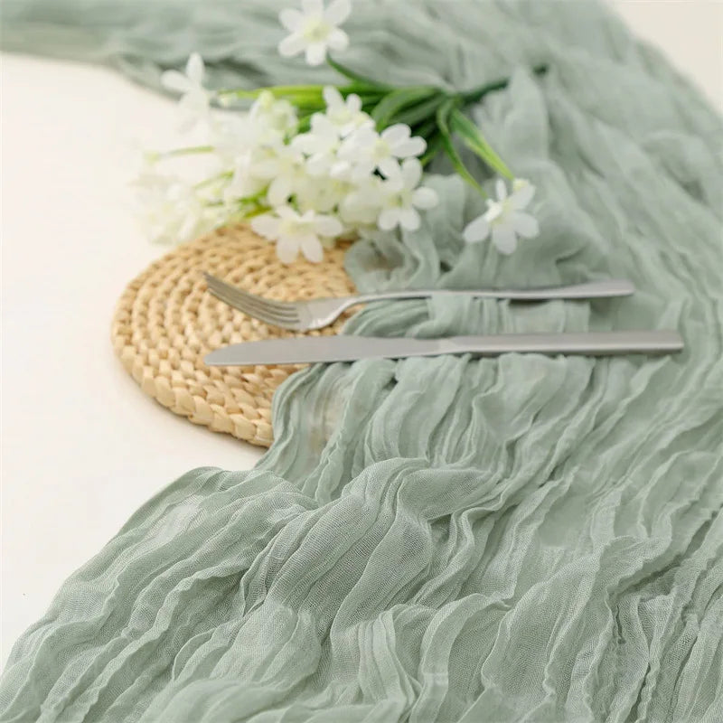 A light green cotton gauze table runner draped with white flowers and silver cutlery.