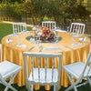 An elegant yellow satin round table set for an outdoor event with white chairs and floral centerpieces.