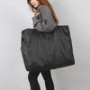 A woman is holding a large black reusable grocery tote with a zipper in front of her.