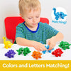 A toddler is playing with a set of dinosaur letter and number matching toys on a white surface.