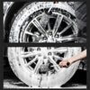 A close-up black and white photo showing a hand using a cleaning brush to clean a silver wheel rim.
