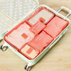 A light green packing cube set with six pink and beige fabric pouches is shown open on a wooden surface.