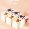A hand holds an open wooden box containing a scary spider trick toy