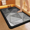 A black bathroom mat with a gray geometric pattern placed on a tiled floor next to a bathtub.