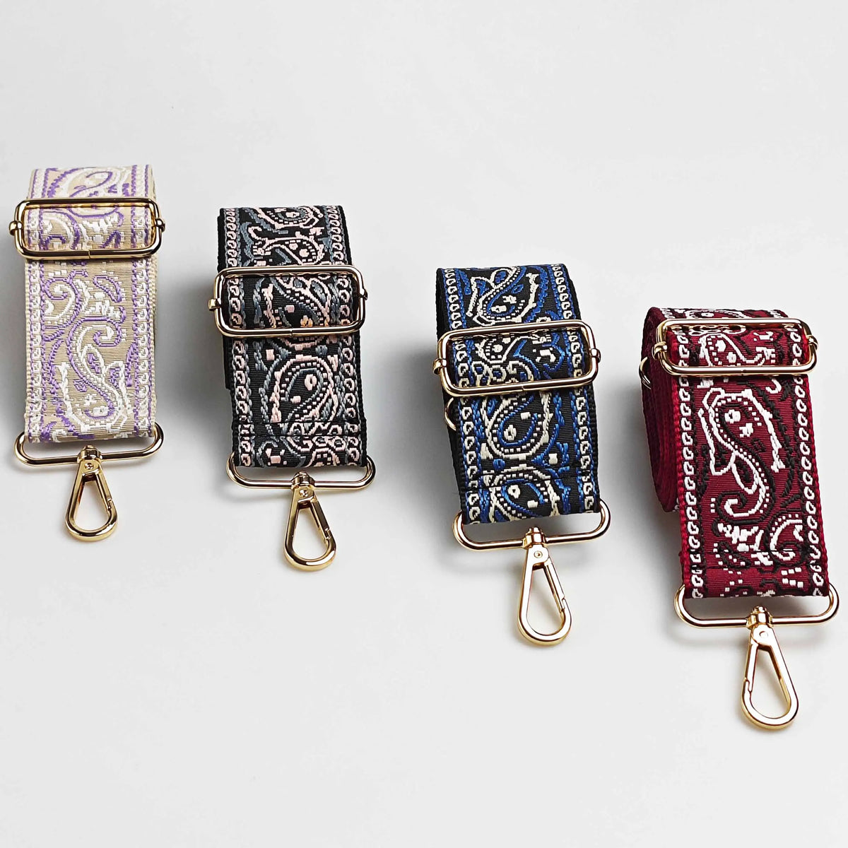 Four adjustable wide paisley jacquard bag straps in purple, black, blue, and red.