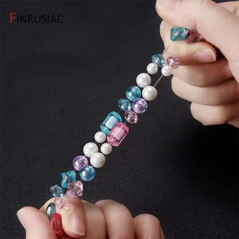 A hand is threading colorful, transparent elastic cords with various gemstone beads for jewelry making.