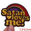 A black and red embroidered patch featuring the text Satan loves me in yellow and purple colors.