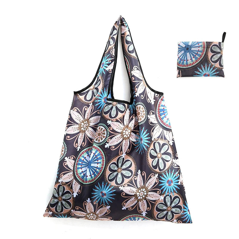 A reusable shopping tote bag featuring a dark background with floral patterns in shades of blue, pink, and beige.