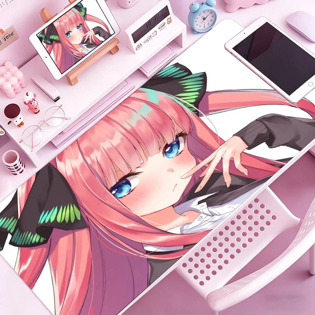 Anime girl illustration featuring pink hair and blue eyes resting on a white mouse pad with various desk accessories.