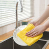 A hand is holding a yellow microfiber cleaning cloth over a sink, next to a kitchen faucet and window blinds.