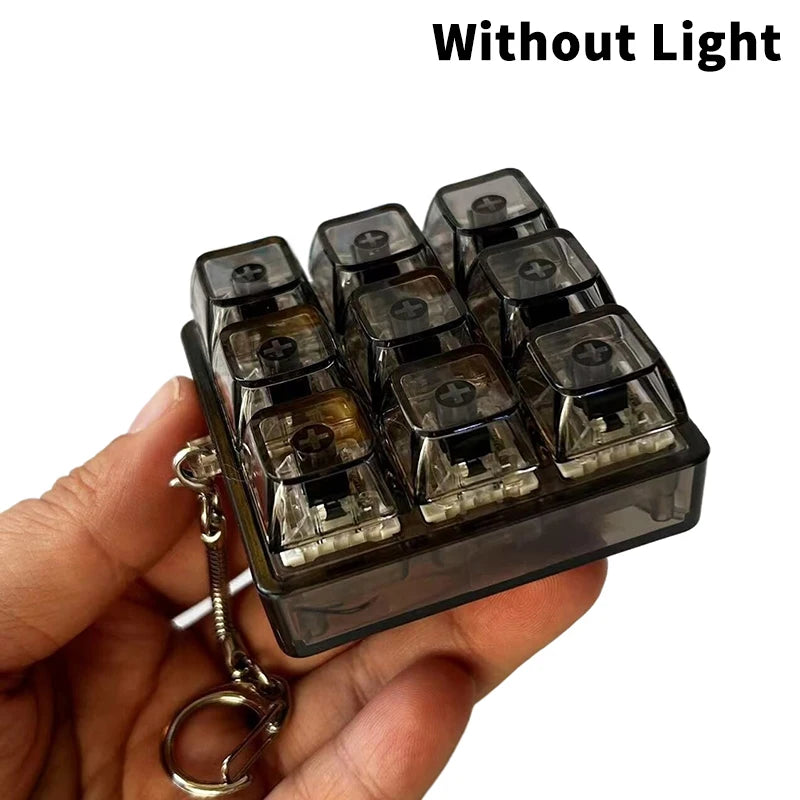 A hand holds a clear plastic keychain fidget toy with multiple black keycaps, shown without light.