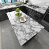 A kitchen countertop made of white and gray marble with a slice of cake and a bowl of green apples.