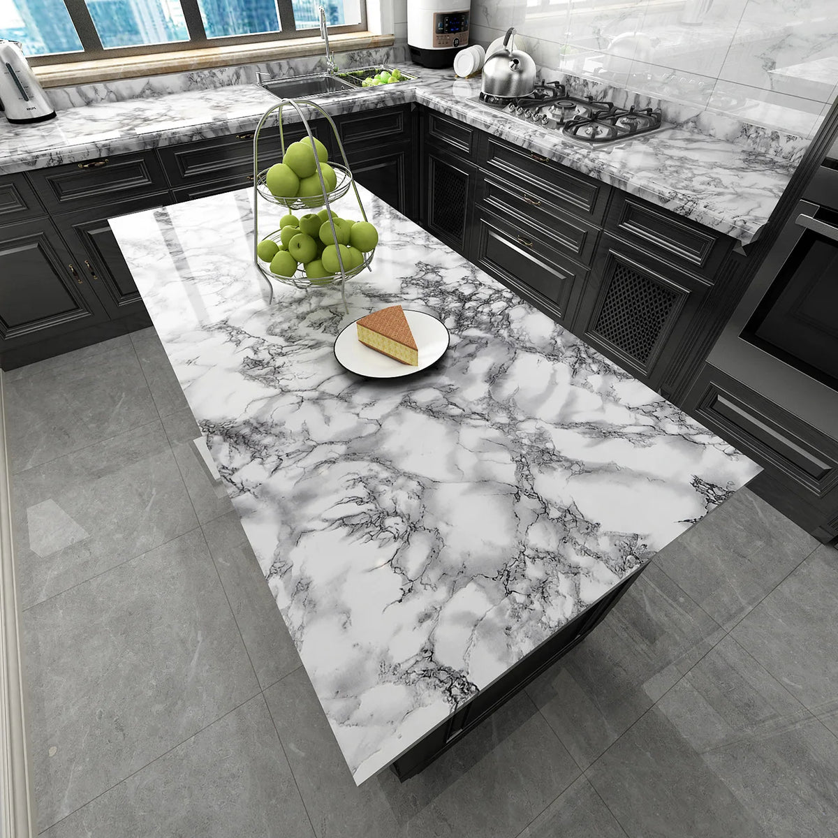 A kitchen countertop made of white and gray marble with a slice of cake and a bowl of green apples.