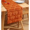 Orange knitted pumpkin pattern table runner laid on a wooden dining table.