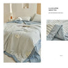 A light blue and white striped breathable summer quilt draped on a bed.
