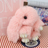 A fluffy pink bunny keychain with a pom pom tail sitting on a patterned surface.