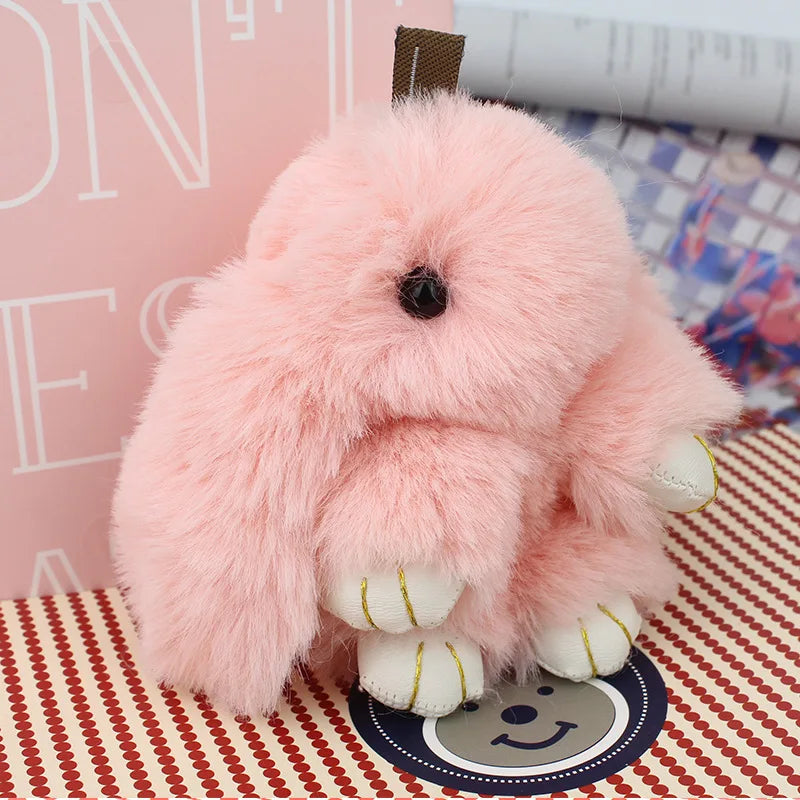 A fluffy pink bunny keychain with a pom pom tail sitting on a patterned surface.