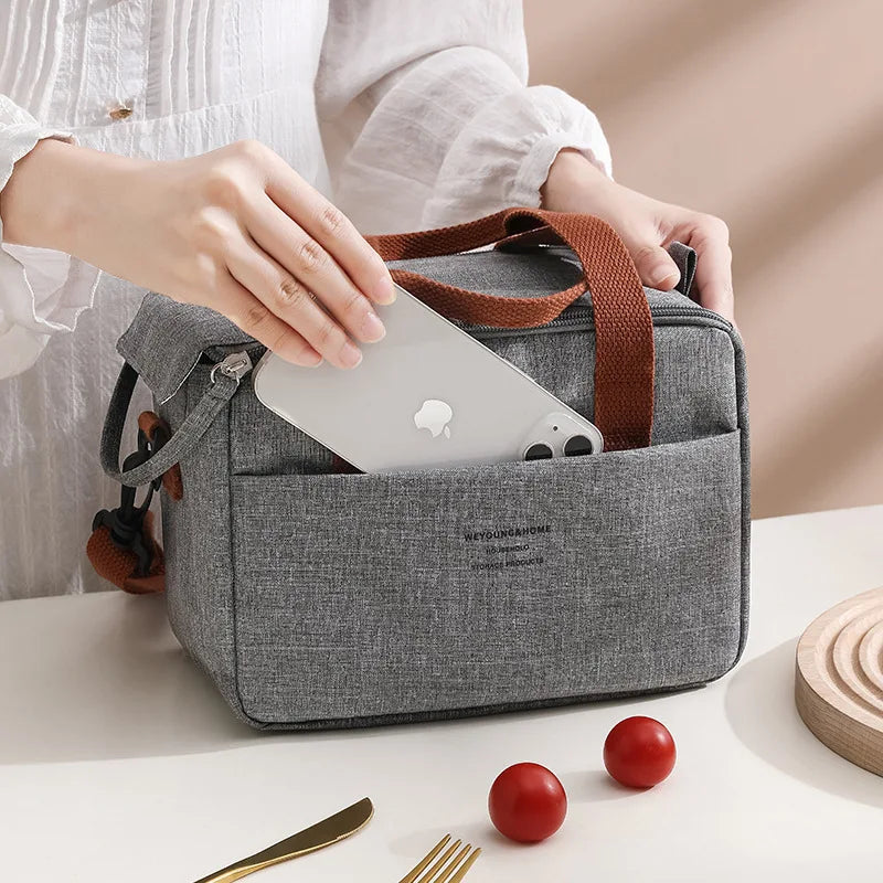 A gray compact thermal lunch tote bag is shown open, holding an Apple device, next to some food items.