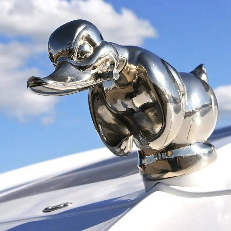 A chrome duck hood ornament is mounted on a white car surface under a blue sky.