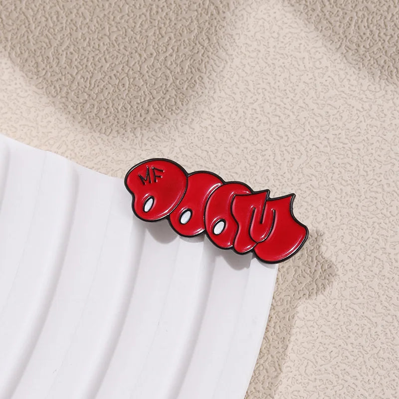 A red enamel pin featuring the text MF DOOM in a bubble font