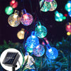 String lights featuring glowing crystal or glass orbs powered by solar panels in an outdoor garden setting