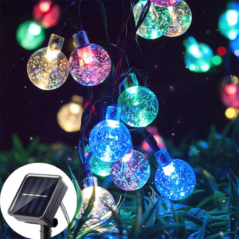 String lights featuring glowing crystal or glass orbs powered by solar panels in an outdoor garden setting