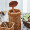 A set of handwoven wicker serving baskets, including a wooden spoon and a large wooden scoop, displayed on a white checkered 