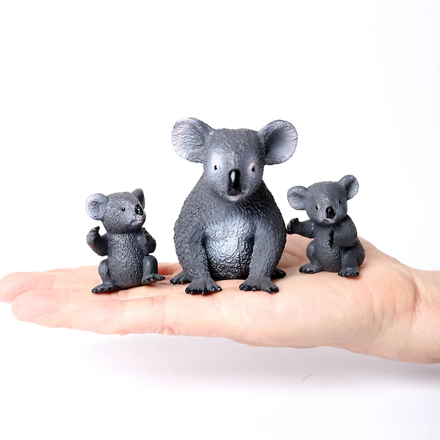 Three realistic grey animal figurines, including a koala, are displayed on a person's palm.
