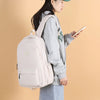 A woman is holding a light beige waterproof nylon laptop backpack while looking at a smartphone.