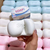 A hand holds a white soap shape fidget toy surrounded by many similar shaped squishy toys.