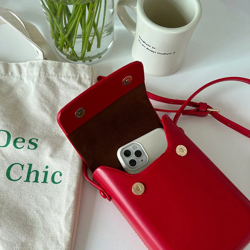 A red vintage PU leather crossbody bag resting on a white surface next to a mug and a linen pouch.