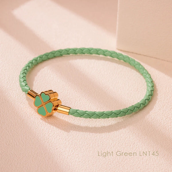 A light green braided leather bracelet with a gold-toned clasp and four-leaf clover charm.